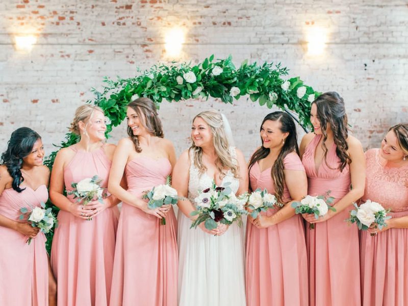 smiling beautiful bride with pretty bridesmaids with brick backdrop