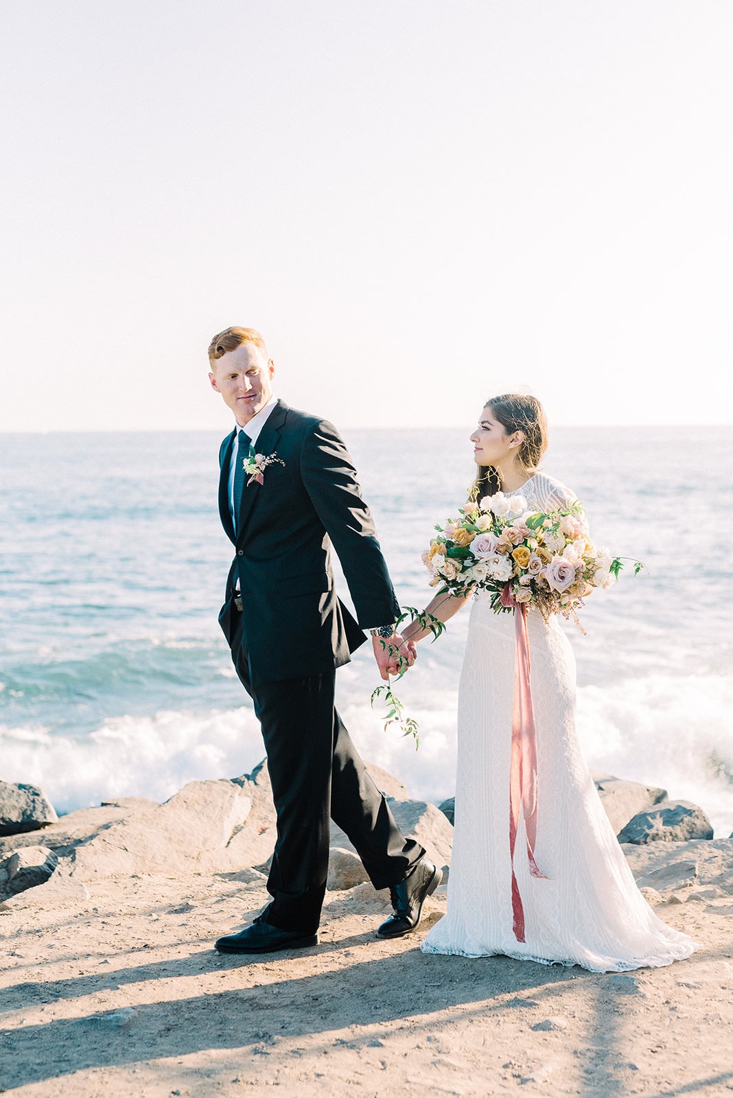 couple holding hands on wedding day by ocean