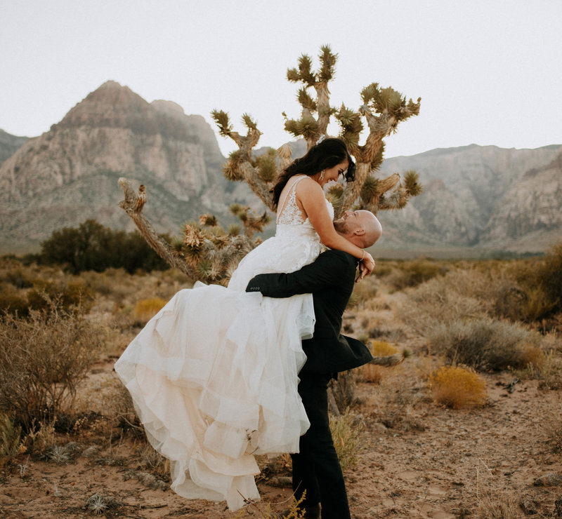groom holding bride up in the air in desert