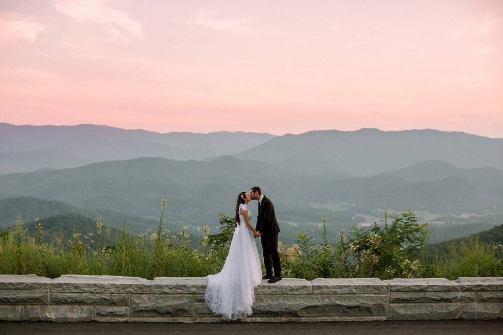 couple taking wedding photo at dusk in the mountains with sunsetting